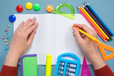 Student writing in school notebook with copy space by pen and school accessories on blue flat lay...