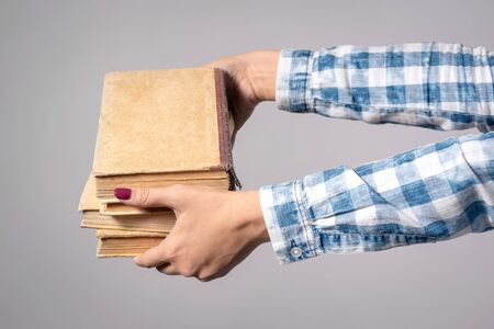 Stack of books in female hands isolated on gray background.の写真素材