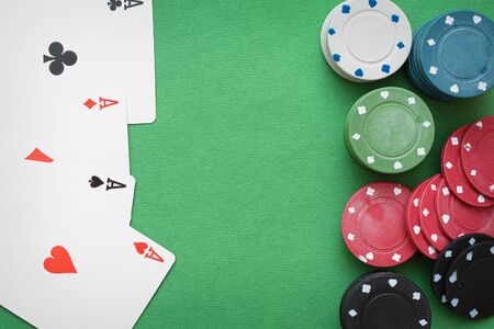 Four aces cards and poker chips on the green table background with copy space.