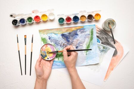An amateur painter is drawing a picture by gouache paint on white table flat lay background close up.の写真素材