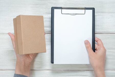 Cardboard box a postal parcel in female hands and blank document with copy space on a clipboard over...