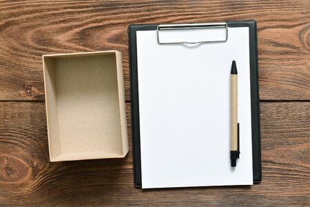 Postal cardboard box and blank page document with a pen on the brown table background.