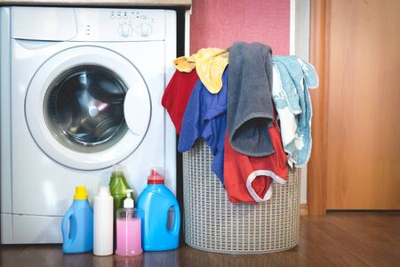 Washing machine, laundry detergent bottles and a dirty clothes in a basket.の写真素材