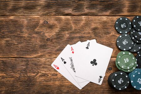Poker chips and four aces cards on wooden table background.