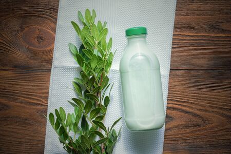 Pistachio milk in a bottle and green pistachio tree branch with green leaves on wooden table background.の写真素材