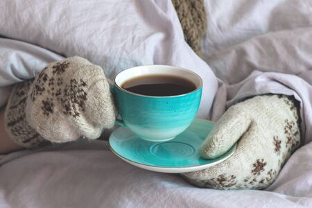 Flu sick woman in mittens warms up with hot tea with lemon.
