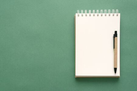 Notepad with a blank pages and pen on a green background.