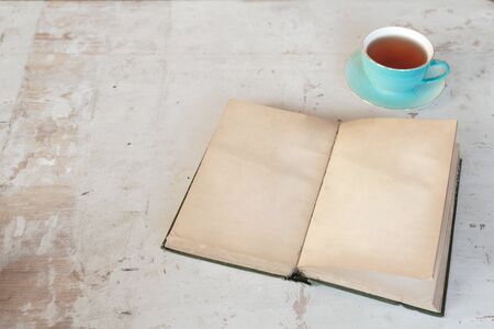 Open blank page book with a copy space and cup of tea on a old white wooden table background.