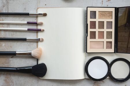 Open blank page notebook template, make up brushes and a eye shadows palette on a white wooden table flat lay background.の写真素材