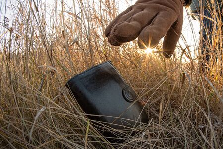 Lost wallet in a grass on the ground outdoors and female hand picking up it from a ground. Close up....