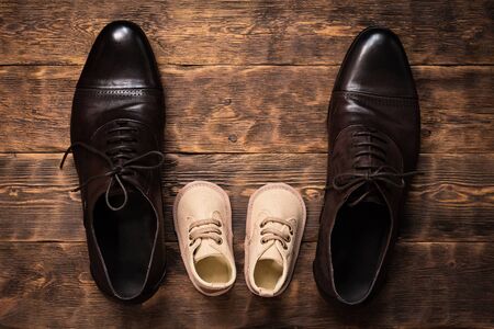 Father shoes and baby booties on a wooden floor.の写真素材