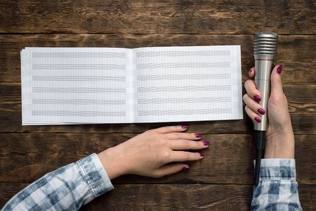 Music book and microphone in female hands on wooden table background.の写真素材