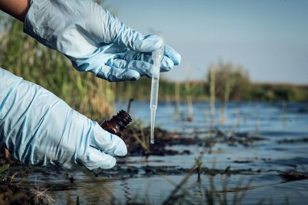 Water pollution concept. Woman scientist takes a water sample from polluted pond.