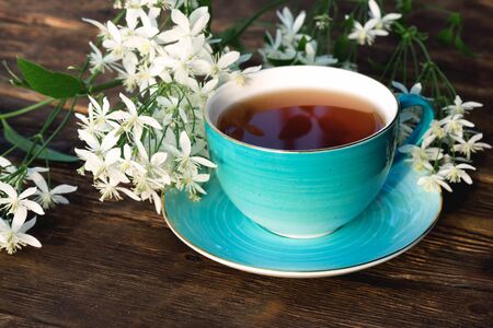 Cup of hot tea and blooming white flowers on a brown wooden table background.の写真素材