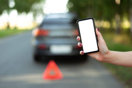 Mobile phone with blank screen on a broken car background. Tow truck service or car repair service...