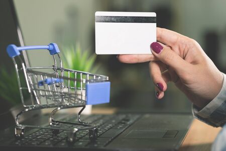 A woman buys goods in an online store. Female hands is holding a credit card on a laptop background.の写真素材