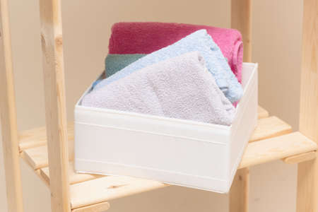 Bath towels in a storage box on wooden rack shelf close up.