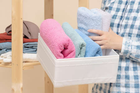 Woman is placing a bath towels in a storage box close up.の写真素材