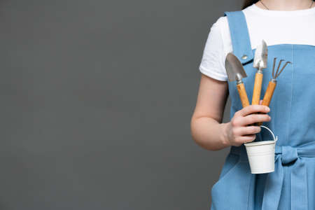 Gardener with garden rake, shovel and small bucket and hands close up on gray background with copy space.の写真素材