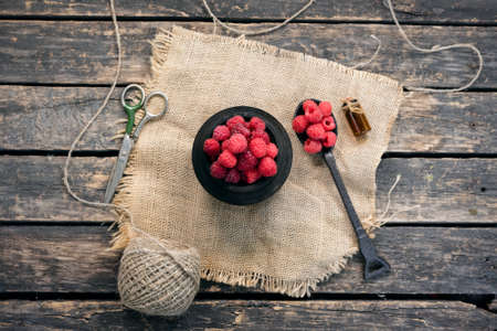 Ripe raspberry fruits in a jar on burlap cloth on an old rural kitchen table background.