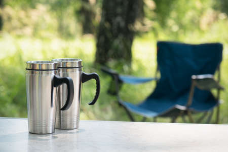 A steel tourist cup on the table on green forest background.の写真素材