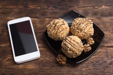 Meringues with butter cream and nuts and blank screen mobile phone on a wooden table background.