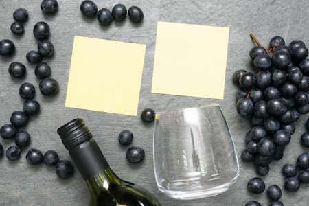 Wine glass, bottle, black grapes and blank paper sheets on stone table surface flat lay background.の写真素材