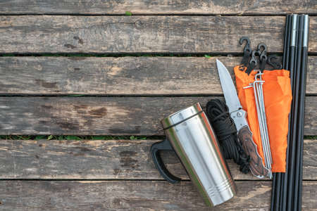 Stainless cup, knife, parts of tent and rope on the wooden table background with copy space.の写真素材