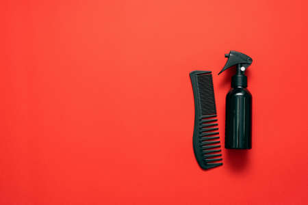 Black hairdressing tools a hair brush and sprayer on the red flat lay background with copy space.の写真素材