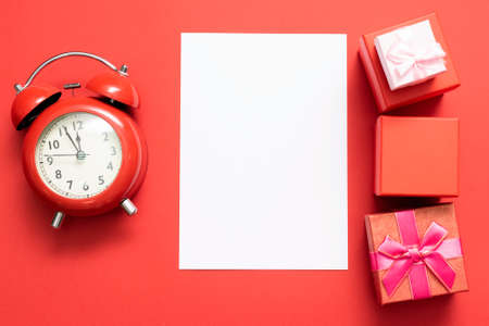 Blank letter page with copy space, red alarm clock and gift boxes on the red flat lay background. Congratulatory letter template.の写真素材