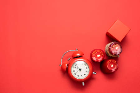 Red alarm clock, gift box and burning candles on the red flat lay background.の写真素材