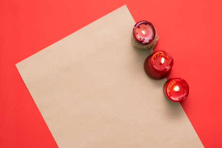A blank paper page and burning candle on the red flat lay background.