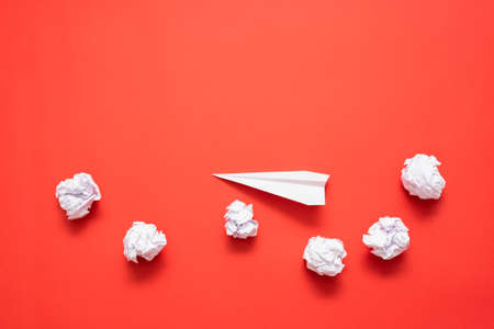 Paper airplane and crumpled paper balls on the red flat lay background.