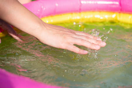 Woman checking the water temperature in the children inflatable pool with her hand close up.