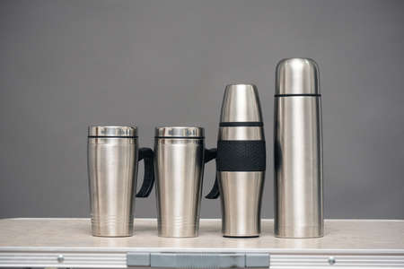 Stainless cups and vacuum flasks on the table on the gray background with copy space.
