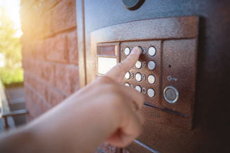 Female finger is pressing on the house intercom button close up.