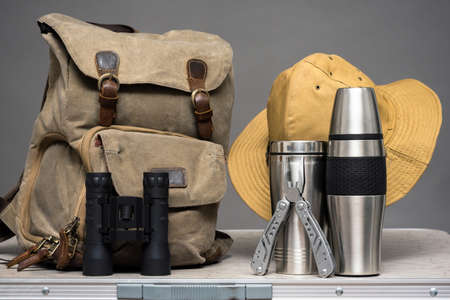 Tourist backpack, binoculars, stainless cup, vacuum flask, hat and multi tool on the traveler table background.の写真素材