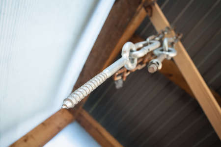 Fixing bolt hanging on the chain on the wooden beam under the house ceiling.の写真素材
