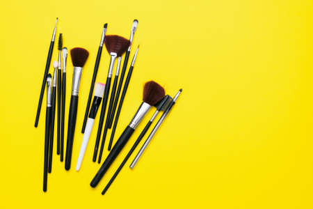 Various black makeup brushes on the yellow flat lay background with copy space.の写真素材