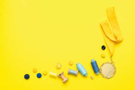 Best tailor or best sewing atelier concept. Sewing accessories and golden award medal on the yellow flat lay background with copy space.の写真素材