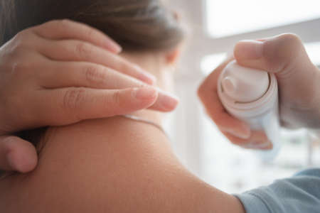 Woman is spraying her neck with the pain reliever spray close up.