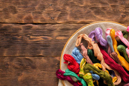 Hoop and colorful threads on the brown wooden table background.