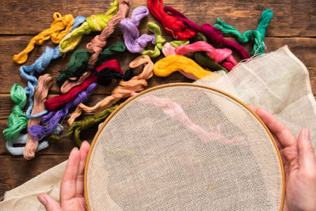 Hoop and colorful threads on the brown wooden table background.