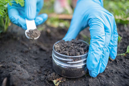 A soil science concept. Scientist is holding in hands a jar with soil sample and scoop.の写真素材