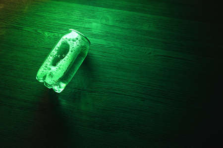 A transparent soda can in the neon lights on the black table background.