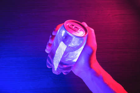 A transparent soda can in the neon lights on the black table background.