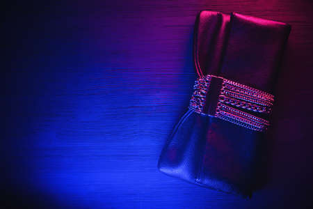 Black leather clutch bag on the black table background in the red blue neon light.の写真素材