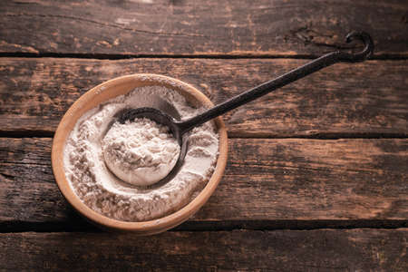 A flour in the iron scoop on the brown wooden table background.の写真素材