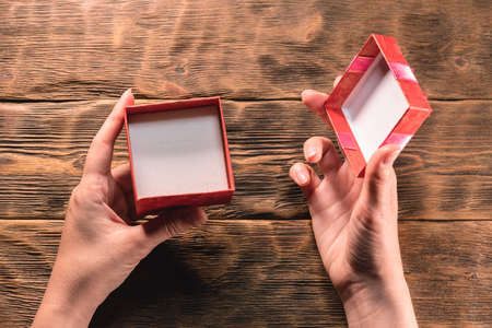 An open empty gift box and female hands on the wooden table background. No gift concept.