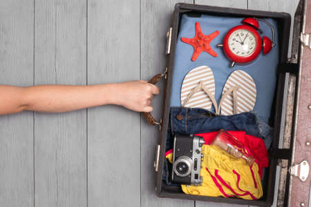 Female hand and old retro suitcase with clothing on the wooden floor background. Top view.の写真素材